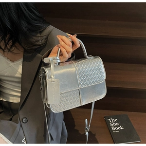 Detail of silver metallic handbag with woven texture and top handle on wooden steps