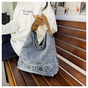 Close-up of vintage blue denim tote bag with FASHION embroidery on a wooden bench