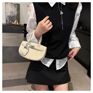 Detail of cream crocodile embossed mini handbag with elegant metal clasp and heart charm