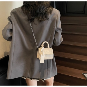 Close-up of off-white woven mini crossbody bag with chain strap on a grey suit model