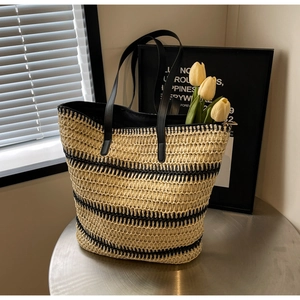 Détail d'un sac cabas en paille tressée avec rayures noires et fines anses en cuir