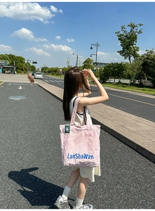 Sac cabas en toile rose avec lettrage bleu et étiquette verte dans un décor extérieur
