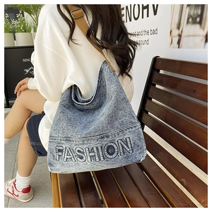 Detail of blue washed denim tote bag featuring fashion embroidery and brown nylon strap