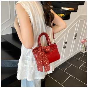 Detail of red patent leather handbag with a polka dot bow knot on a model shoulder