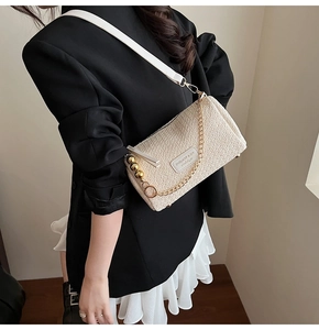 Detail of beige straw texture shoulder bag with gold chain and metal ball charm decoration