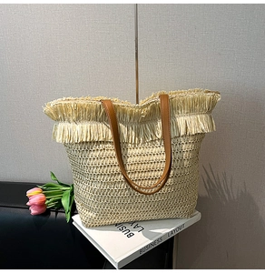 Close-up of woven straw tote bag featuring decorative fringe and brown leather straps