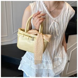 Detail of yellow leather square bag with decorative polka dot scarf and metal buckle