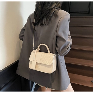 Detail of beige crossbody bag with woven texture and top handle on a neutral background