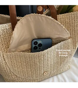 Detail of a straw tote bag front pocket showing storage capacity for a smartphone