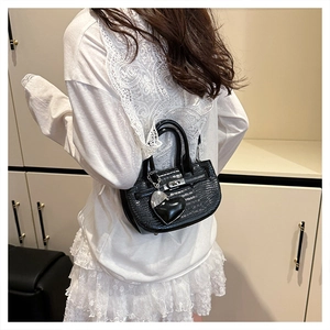 Detail of black croc-embossed leather handbag with heart pendant on white lace dress