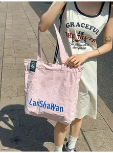 Photo de rue d'un grand sac cabas rose en nylon avec texte bleu et étiquettes vertes