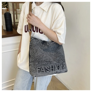 Detailed view of gray washed denim tote bag with embossed fashion logo and wide strap
