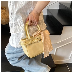 Detail of yellow leather square bag with decorative silk scarf on handle and metal buckle