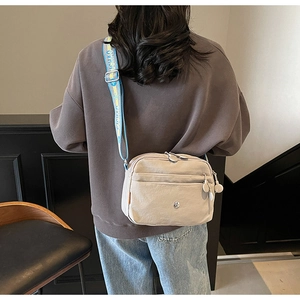 Détail du sac bandoulière en nylon beige avec design multi-poches et sangle imprimée