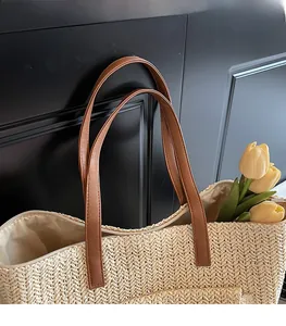 Detail of woven straw tote bag featuring brown leather straps and metal zipper closure
