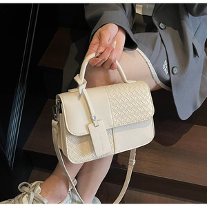 Detail of creamy white woven leather handbag with adjustable strap held by a model
