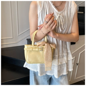 Detail of light yellow square handbag with leather texture and decorative polka dot scarf