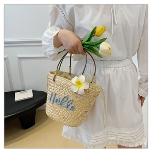 Detail der Strohhandtasche mit blauem Hello-Stick und einer weißen Plumeria-Blüte