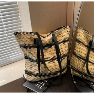 Détail d'un sac cabas en paille tressée avec anses en cuir noir et rayures