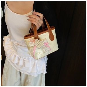 Detail of a mini bucket bag featuring a large lace bow, pearl heart, and pink ribbon accents