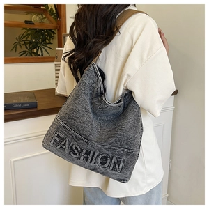 Detail of the washed denim tote bag featuring embossed FASHION lettering and webbing strap