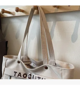 Dettaglio borsa tote in tela beige con cerniera, fibbia metallica e scritte marroni