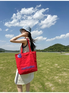 Vue extérieure d'un grand sac cabas en nylon rouge avec lettrage bleu sur l'herbe