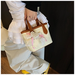 Detail of cream crossbody bucket bag with pearl heart charm and lace bow decoration