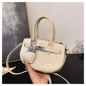 Detail of crocodile embossed mini handbag with metal turn-lock and heart charm accessory