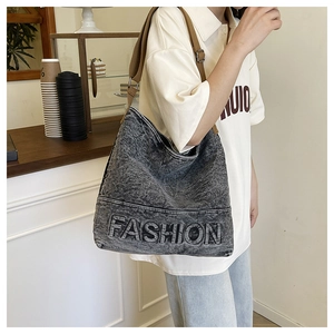 Detail of grey washed denim hobo bag with FASHION embroidery and wide brown strap