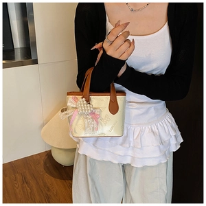 Close-up of butterfly embossed cream bucket bag with lace bow and pearl heart charm
