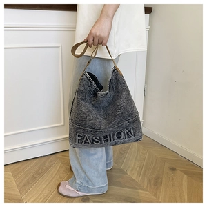Detail of fashion embossed letters on dark grey washed denim tote bag with leather strap