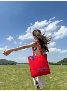 Détail du grand sac cabas en nylon rouge avec étiquette bleue en extérieur sur herbe verte
