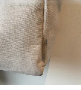 Dettaglio ravvicinato della borsa in tela beige con texture spessa e logo nero cucito