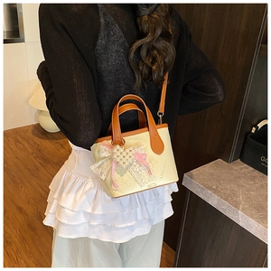 Detail of cream leather bucket bag showing butterfly print and pearl heart pendant charm