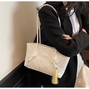 Detail einer beigen Handtasche mit geometrischer Prägung und Quastenanhänger-Dekoration