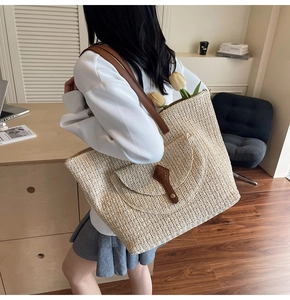 Detail of handwoven straw tote bag with brown leather straps and front pocket detail