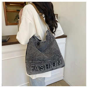 Detail of grey washed denim tote bag featuring embossed FASHION text and brown strap