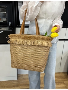 Handwoven straw tote bag with brown leather handles and raffia fringe edge for summer vacations