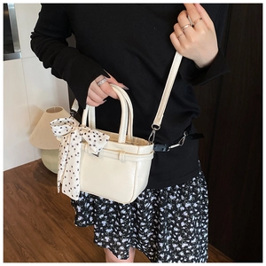 Detail of minimalist cream square bag with polka dot scarf and silver metal buckle hardware