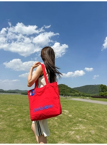Détail du grand sac cabas en nylon rouge avec logo LanShaWan sur fond d'herbe et montagnes