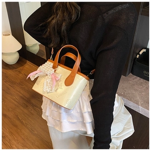 Detail of cream bucket bag featuring butterfly embossing, pearl charm, and pink lace bow