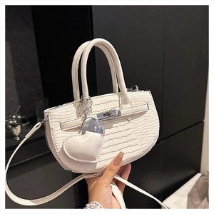 Detail of white crocodile pattern handbag with silver clasp and heart-shaped charm