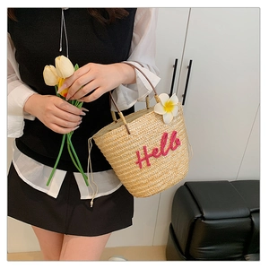 Detail der Stroh-Eimertasche mit rosa Hello-Stickerei und tropischer Blüte