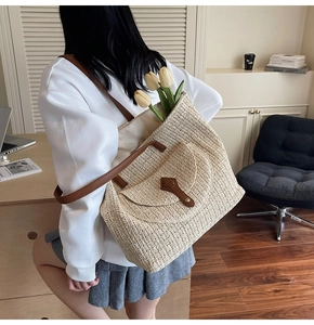 Detail of hand-woven straw tote bag featuring brown leather shoulder straps on a female model