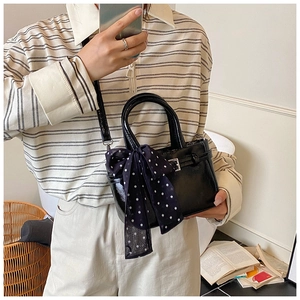Detail of black glossy square bag with polka dot scarf and strap on casual model outfit