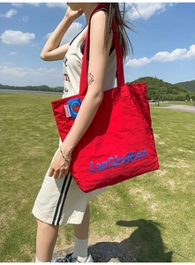 Vue détaillée d'un sac cabas en nylon rouge avec logo bleu et écusson pomme décoratif