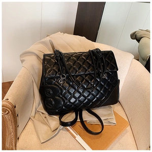 Dettaglio borsa in pelle trapuntata nera con logo B in metallo dorato su una poltrona