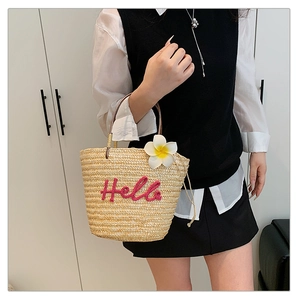 Detail der Strohtasche mit rosa Hello-Stickerei und Frangipani-Blütenverzierung