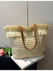 Handwoven straw tote bag with brown leather straps and tassel fringe details